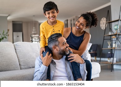 Cheerful African Mother And Indian Father Playing With Son At Home Cute Boy Enjoying Sitting On Father Shoulder While Looking At Camera Middle Eastern Family Having Fun Together On The Sofa At Home