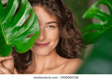 Close Up Face Of Beautiful Young Woman Covering Her Face By Green Monstera Leaf While Looking At Camera Portrait Of Beauty Woman With Natural Makeup And Freckles Standing Behind Big Green Leaves