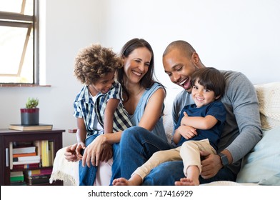 Happy Multiethnic Family Sitting On Sofa Laughing Together Cheerful Parents Playing With Their Sons At Home Black Father Tickles His Little Boy While The Mother And The Brother Smile