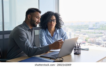 Indian Male Ceo Executive Manager Mentor Giving Consultation On Financial Operations To Female African American Colleague Intern Using Laptop Sitting In Modern Office Near Panoramic Window