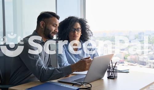 Indian Male Ceo Executive Manager Mentor Giving Consultation On Financial Operations To Female African American Colleague Intern Using Laptop Sitting In Modern Office Near Panoramic Window