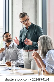 Mature Businessman Leader Mentor Talking To Diverse Colleagues Team Listening To Caucasian Ceo Multicultural Professionals Project Managers Group Negotiating In Boardroom At Meeting Vertical