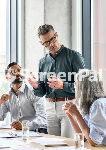 Mature Businessman Leader Mentor Talking To Diverse Colleagues Team Listening To Caucasian Ceo Multicultural Professionals Project Managers Group Negotiating In Boardroom At Meeting Vertical