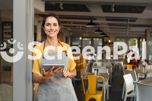 Portrait Of Happy Woman Standing At Doorway Of Her Store Cheerful Mature Waitress Waiting For Clients At Coffee Shop Successful Small Business Owner In Casual Wearing Grey Apron Standing At Entrance