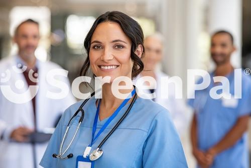 Portrait Of Happy Young Nurse In Uniform With Healthcare Team In Background Successful Team Of Doctor And Nurses Smiling Beautiful And Satisfied Healthcare Worker In Private Clinic Looking At Camera