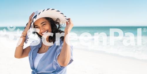 Portrait Of Stylish Latin Hispanic Woman With White Straw Hat Standing At Beach Young Smiling Woman On Vacation Enjoy Sea Breeze Wearing Straw Hat And Looking At Camera Attractive Beautiful Girl