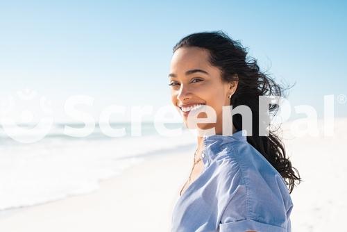 Portrait Of Young Woman At Sea Looking At Camera Smiling Latin Hispanic Girl Standing At The Beach With Copy Space And Looking At Camera Happy Mixed Race Girl In Casual Outfit With Wind In Her Hair