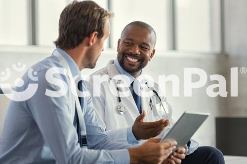 Two Mature Smiling Doctors Having Discussion About Patient Diagnosis Holding Digital Tablet Representative Pharmaceutical Discussing Case After Positive Result With Happy Doctor About New Medicine