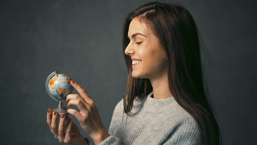 Beautiful Dark Haired Girl In Warm Grey Sweater Turning The Globe Indoor Isolated Shot