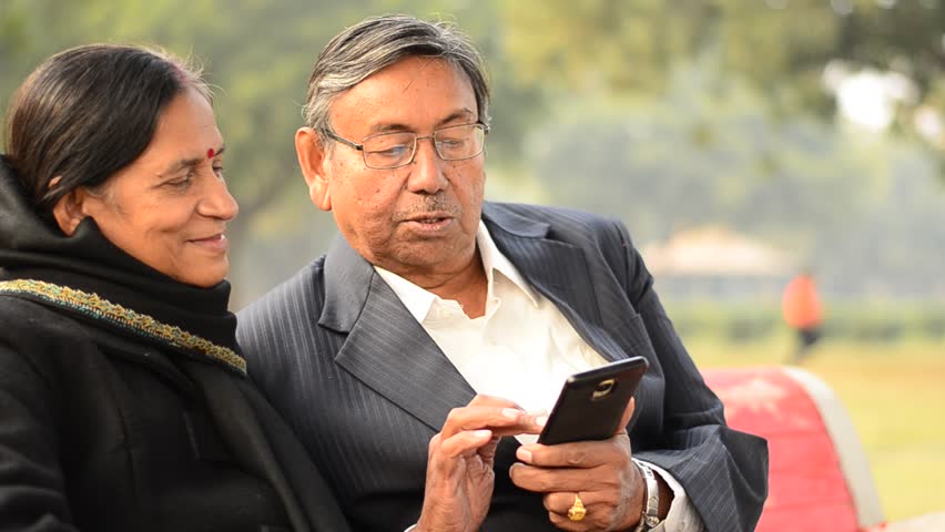 Senior Citizen Couple Reading From  Working On A Mobile Reading Jokes And Talking Smiling Laughing  In A Park In Delhi India