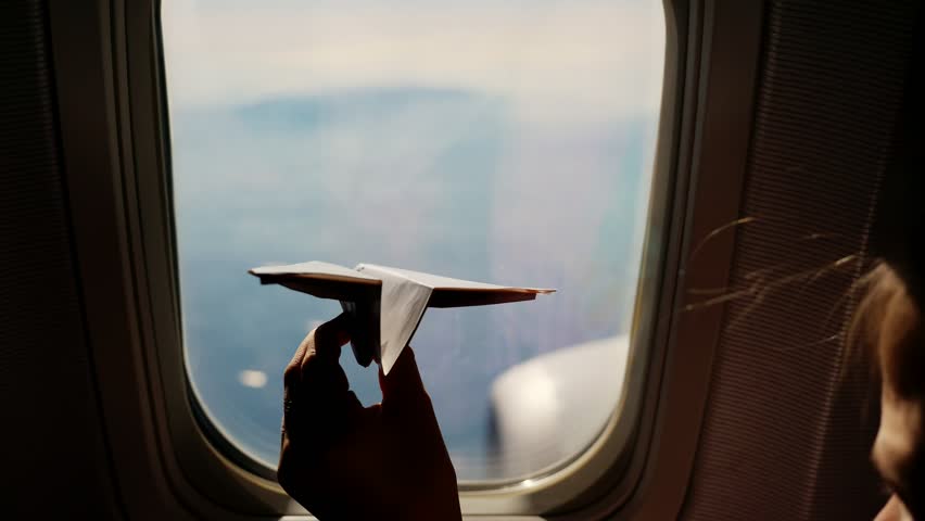 Close Up Silhouette Of A Childs Hand With Small Paper Plane Against The Background Of Airplane Window Child Sitting By Aircraft Window And Playing With Little Paper Plane During Flight On Airplane