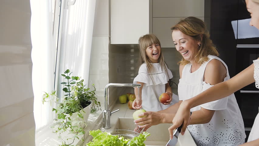 Young Caucasian Mother With Her Daughter Is Having Fun Splashes Each Other Water In The Kitchen And Wash The Vegetables For Ready To Cook Salad For Lunch Slow Motion