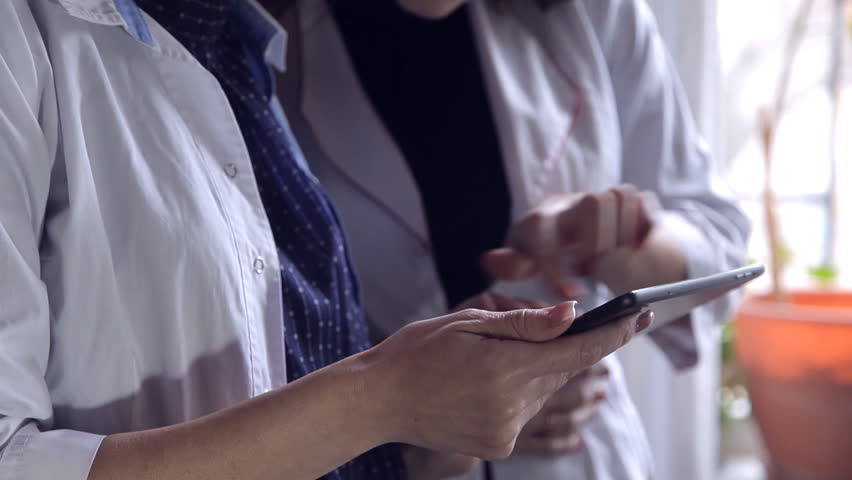 Two Female Doctors Look Through Medical Notes In A File And Consult On Diagnosis Intelligent Professional Healthcare Workers White Caucasian Young Adults