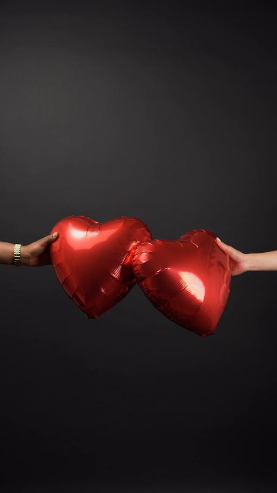 Two Persons Holding Two Red Heart Shaped Balloons