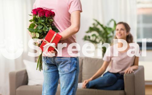 Couple Relationships And People Concept   Happy Woman Looking At Man Hiding Flowers And Gift Behind His Back At Home