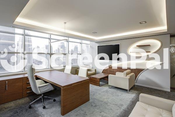 Gray Office Rolling Chair Near Brown Wooden Desk In Front Of Flat Screen Tv On White Painted Wall