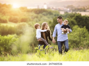 Happy Young Family Spending Time Together Outside In Green Nature