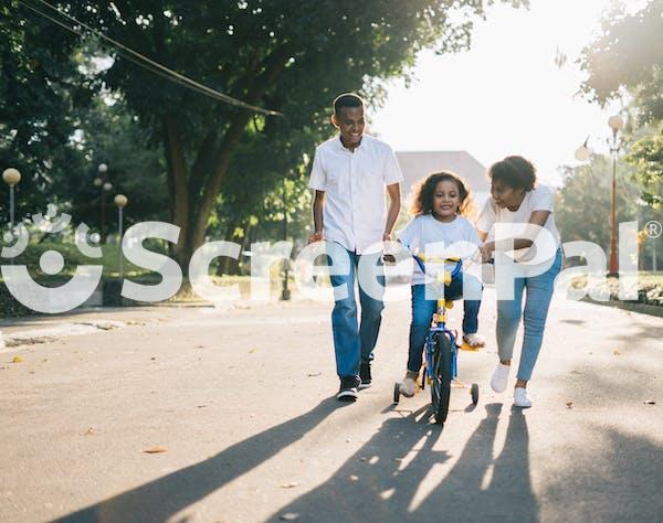 Man Standing Beside His Wife Teaching Their Child How To Ride Bicycle