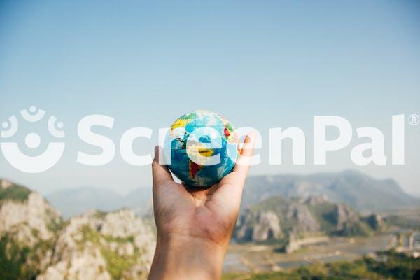 Person Holding World Globe Facing Mountain